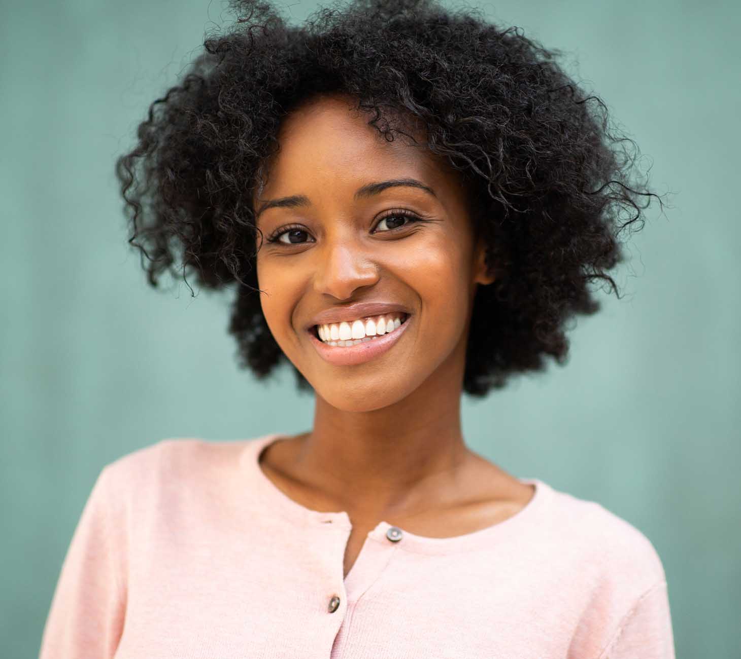 A black women smiling whilst looking directly after her consultation, where she looked to compare the treatments dental implants and Dentures